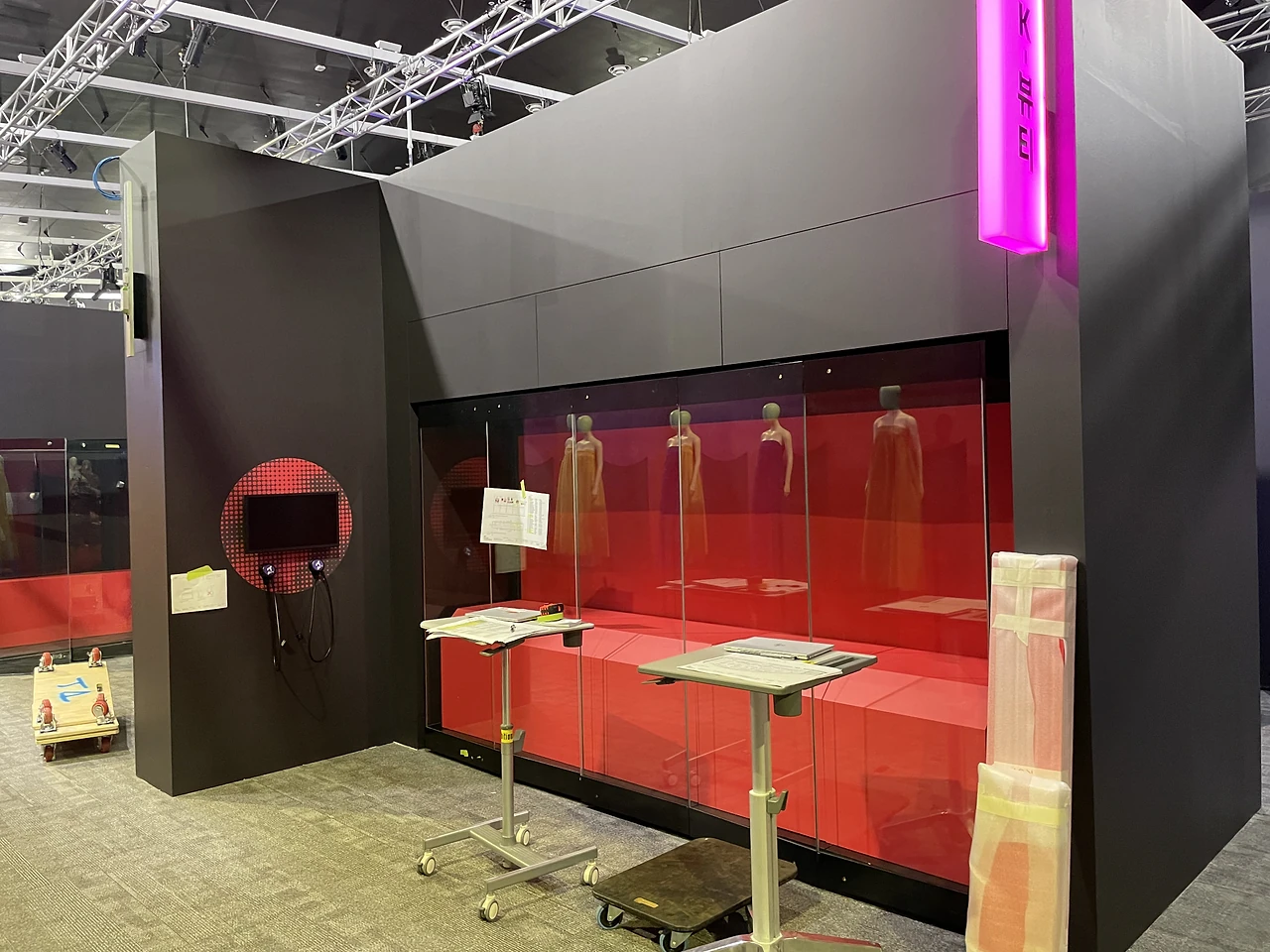 Glazed red-backed showcase with gowns and a pink neon sign above black walls