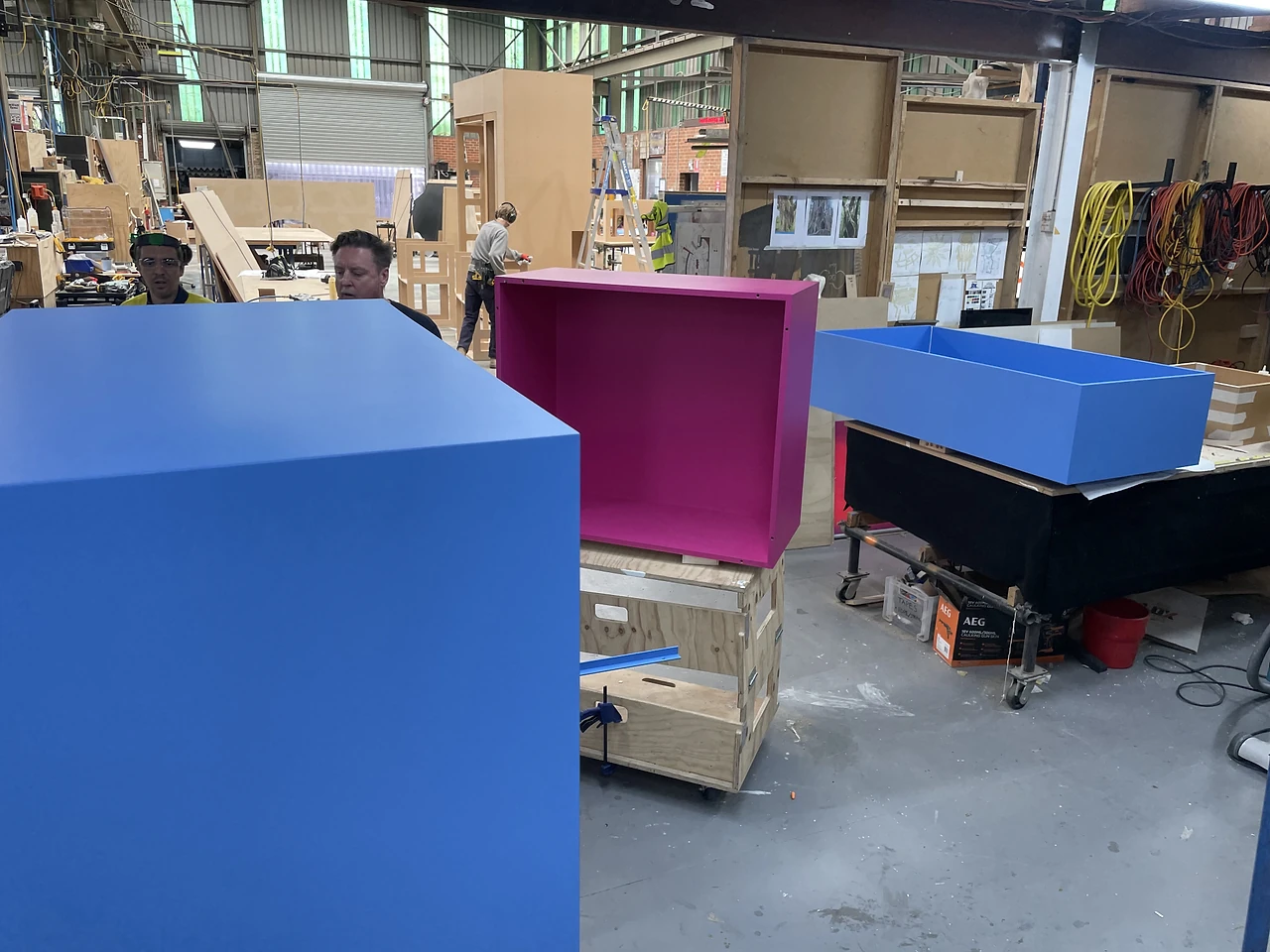Blue and magenta painted display boxes on trolleys in the workshop