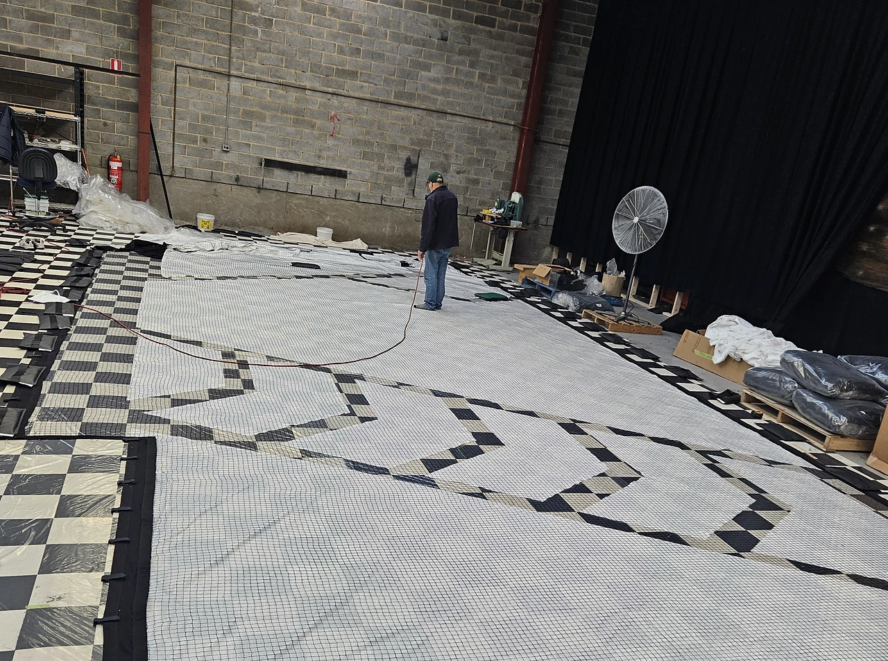 Net backdrop panels spread across a checkerboard floor with a crew member checking the layout