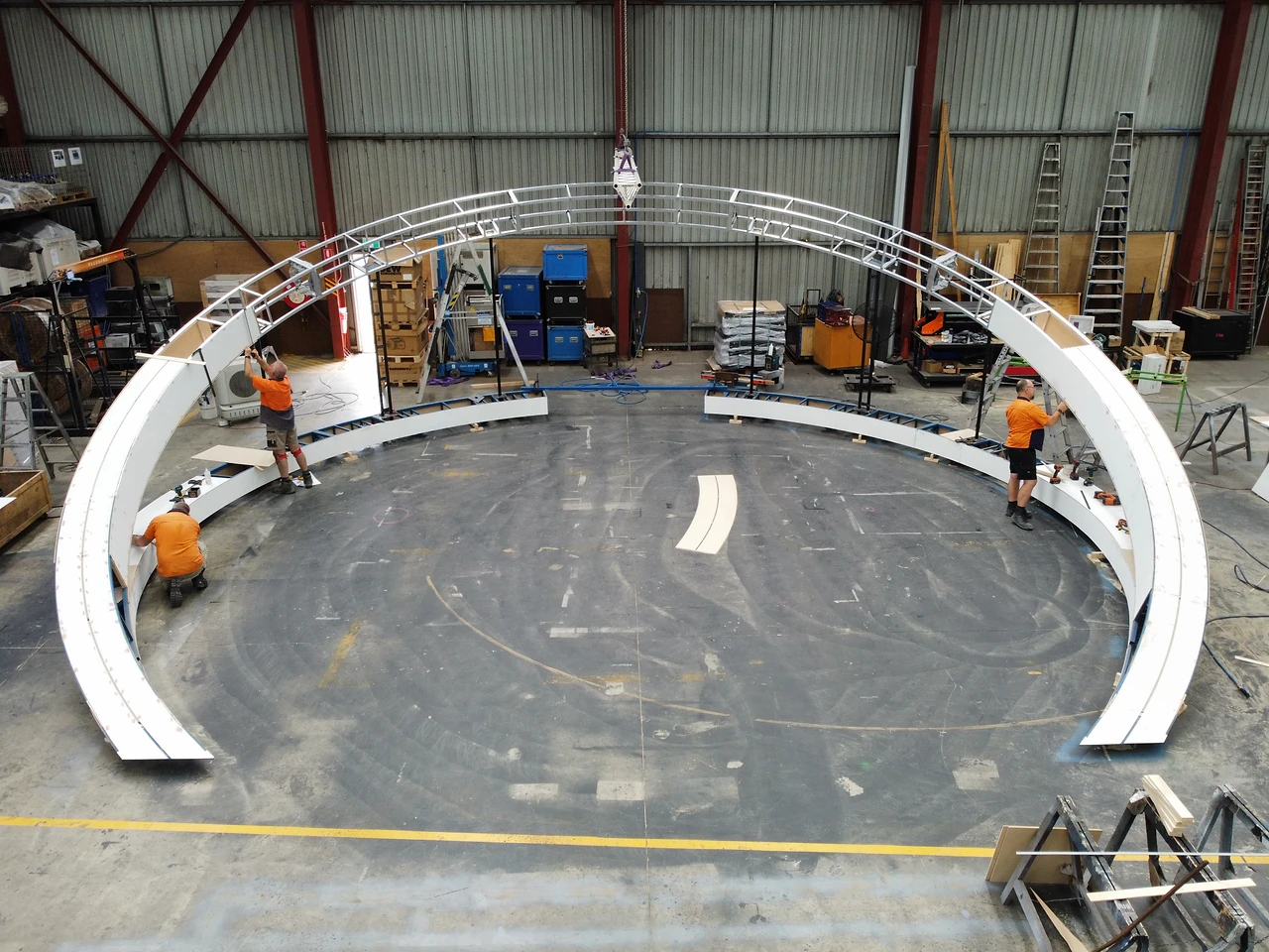 Two crew members assembling curved white ring segments on a steel base track