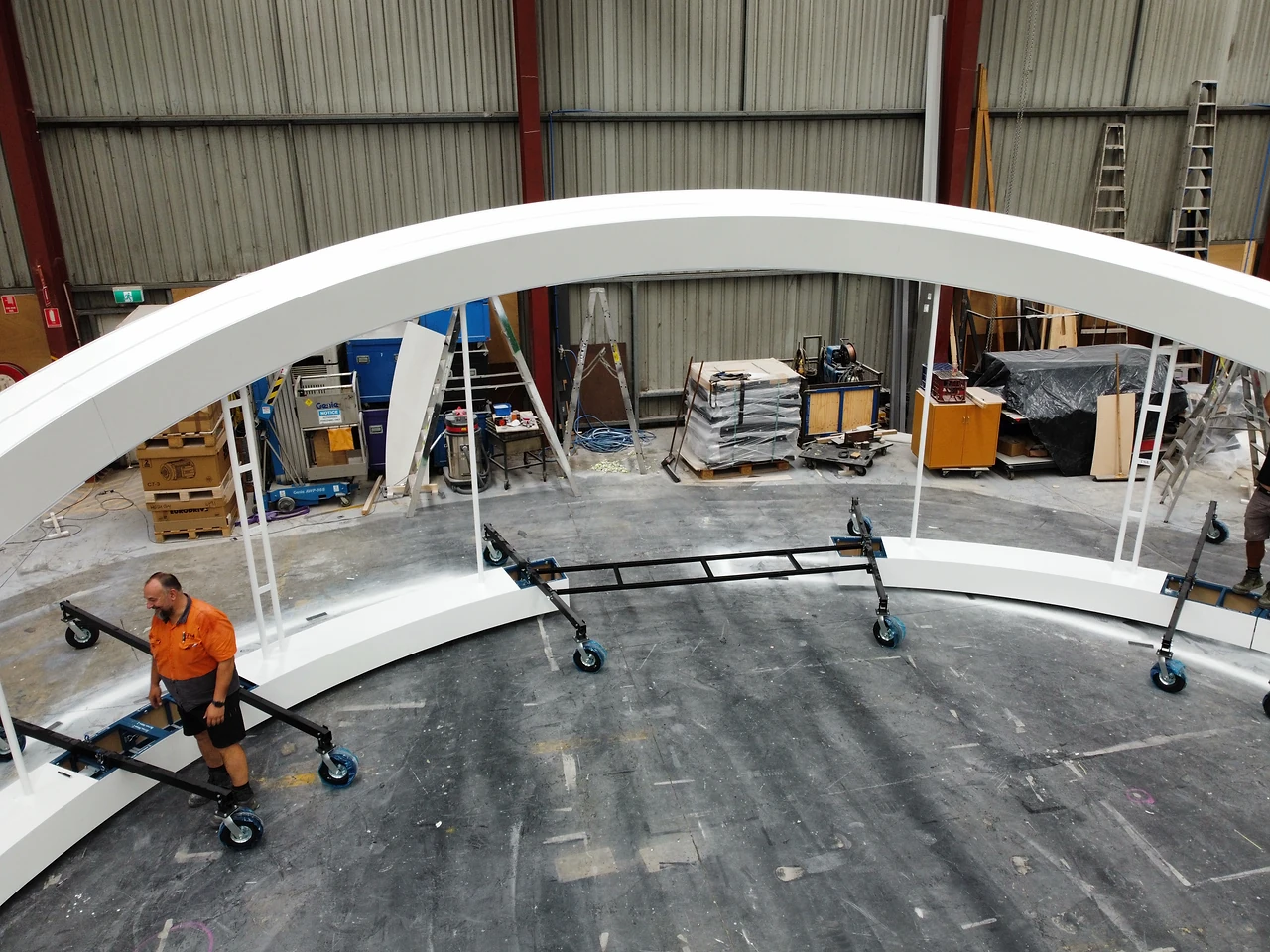 Crew carrying arch sections on wheeled steel dollies beneath the finished white arch