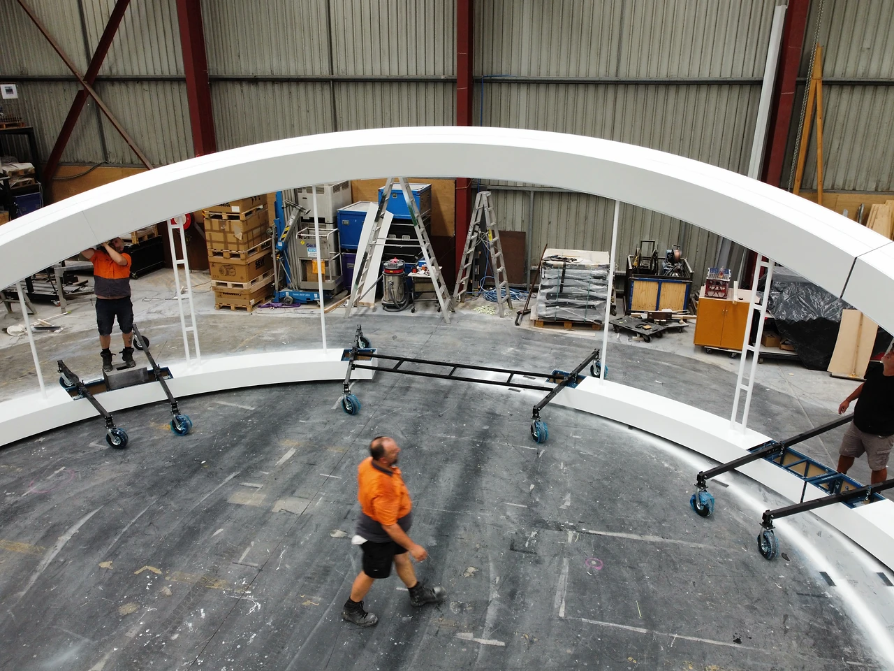 Smooth white arch spanning the workshop with crew positioning the next segment