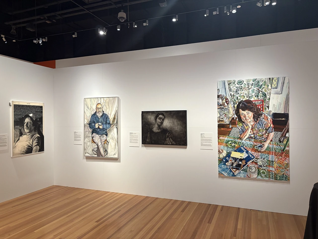 Finished white gallery wall lit by track lights, its panel joints showing as fine lines, with portrait works hung along it at the Brisbane Portrait Prize 2026. Design: Tim Blaikie, TSA. Photo: TSA. Artworks by various artists, Brisbane Portrait Prize 2026.