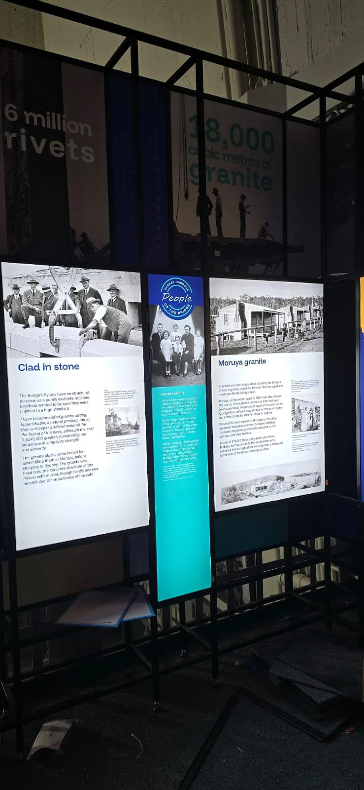 Lit interpretive display with steel frame, archive photos and rivet statistics inside the pylon