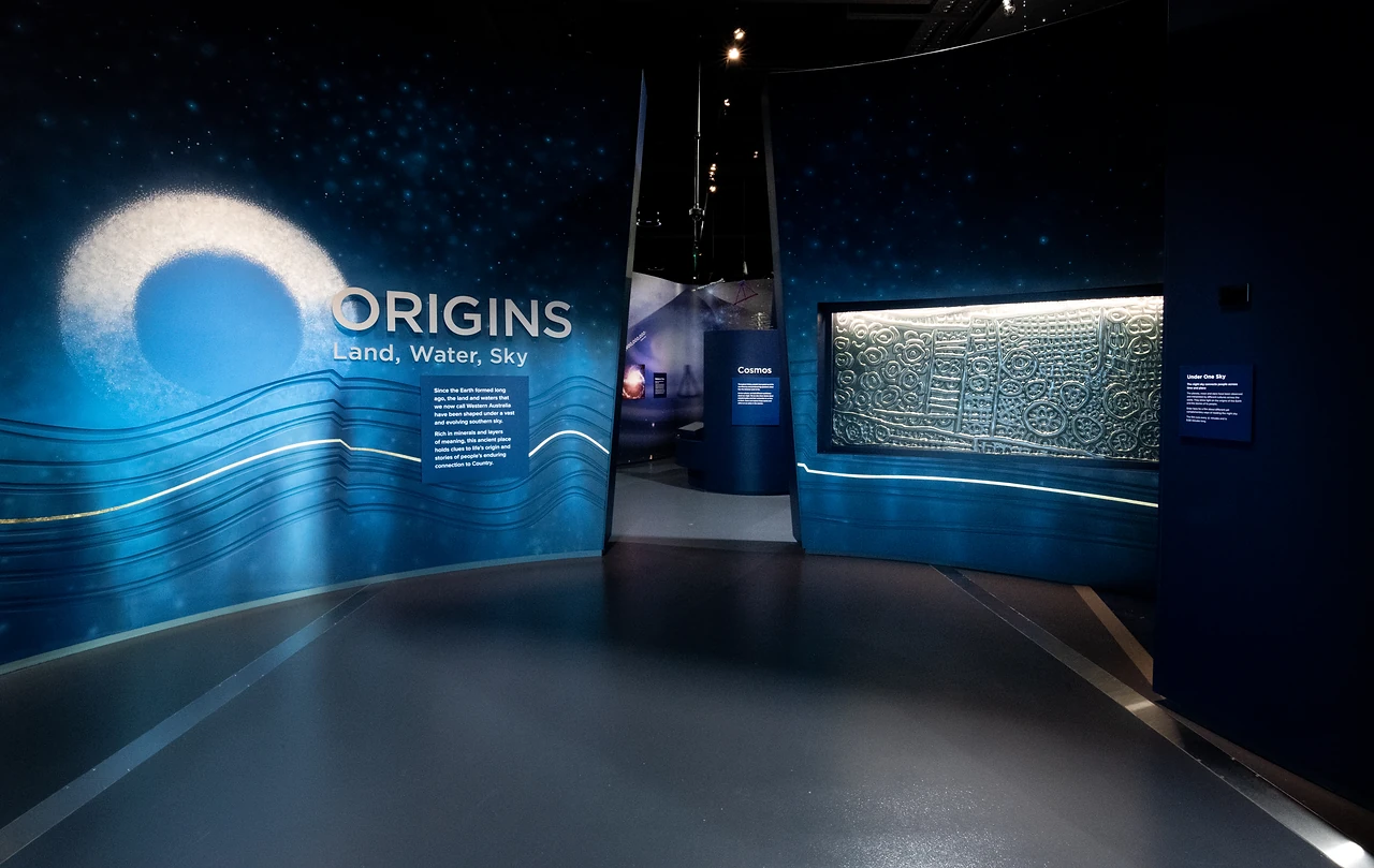 Origins gallery entry wall with the ORIGINS title lettering over an orange scenic panel and curved joinery. Design: Thylacine Design with Iredale Pedersen Hook architects. Photo: Michelle Sammut.