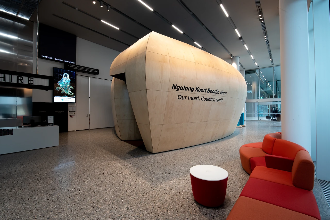 Sculpted timber pod in the museum foyer carrying the Ngalang Koort Boodja Wirn title, with red upholstered seating beside it. Design: Thylacine Design with Iredale Pedersen Hook architects. Photo: Michelle Sammut.
