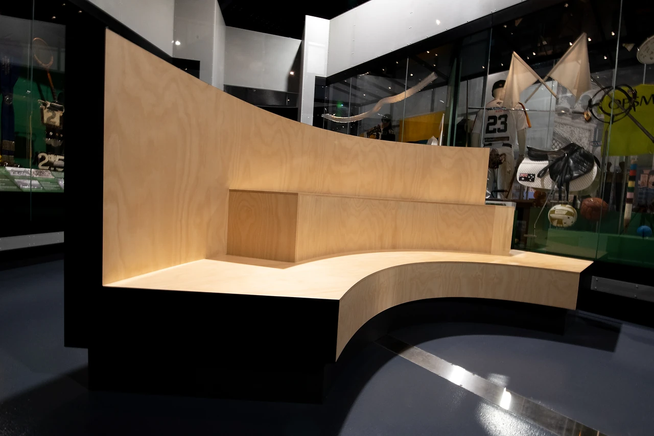 Curved plywood bench with a sweeping backrest in the Reflections gallery, with showcases behind. Design: Thylacine Design with Iredale Pedersen Hook architects. Photo: Michelle Sammut.
