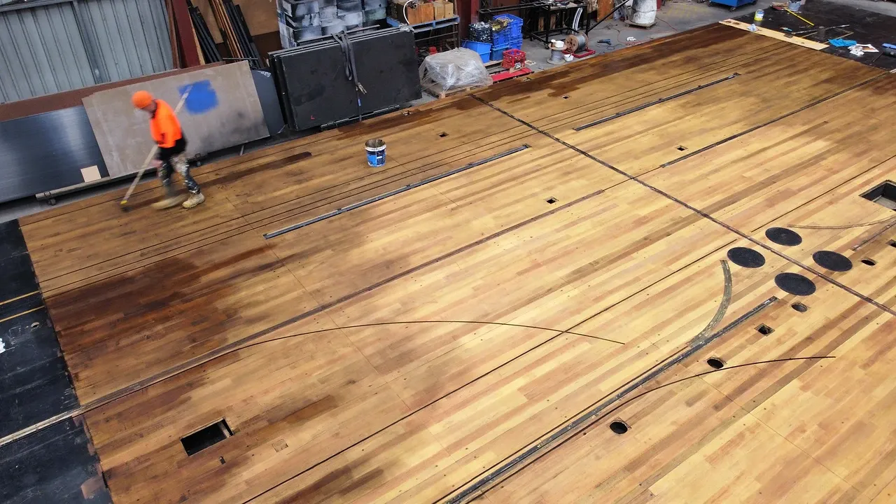 A TSA crew member staining the sanded Wicked show deck in the workshop, fresh dark finish sweeping across the timber.