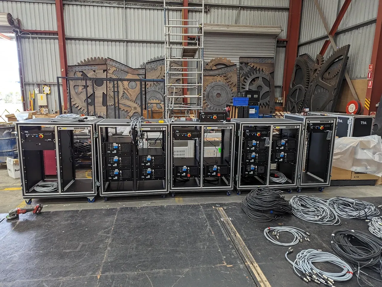 Five TSA-built automation drive racks lined up in the workshop, coiled looms in the foreground and Wicked scenery behind.