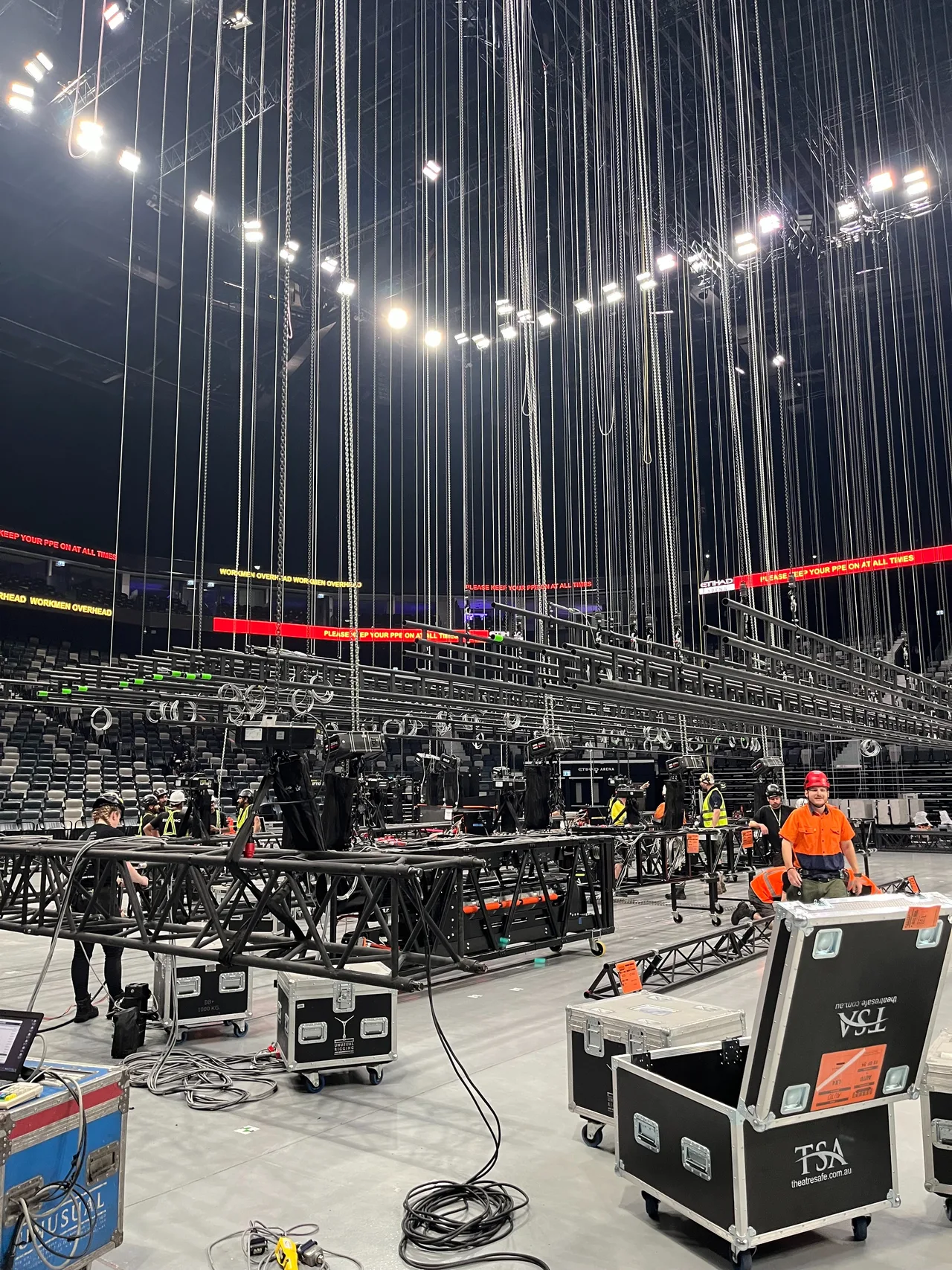 Arena load-in with chain hoist drop lines from the roof grid and truss sections on the floor